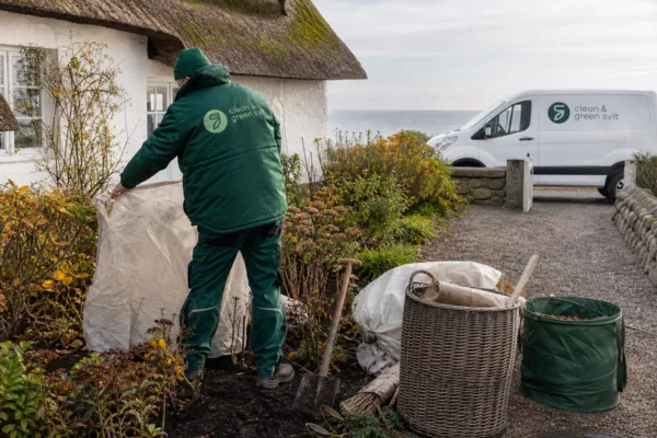 Ein Gartenarbeiter deckt im Herbst auf Sylt Beete an einem Reetdachhaus ab.