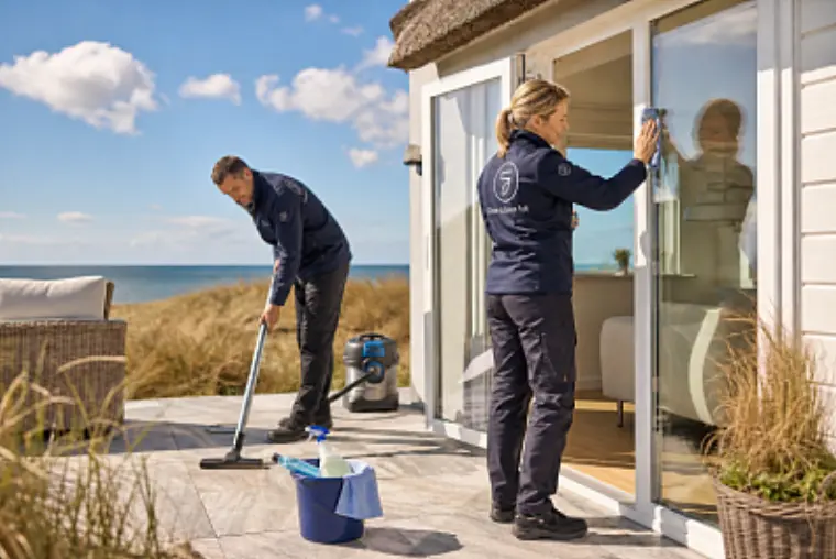 Reinigungsteam bereitet ein helles Ferienhaus auf Sylt mit Terrasse und Glasfront für die Übergabe vor.