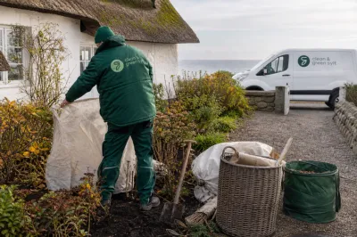 Ein Gartenarbeiter deckt im Herbst auf Sylt Beete an einem Reetdachhaus ab.